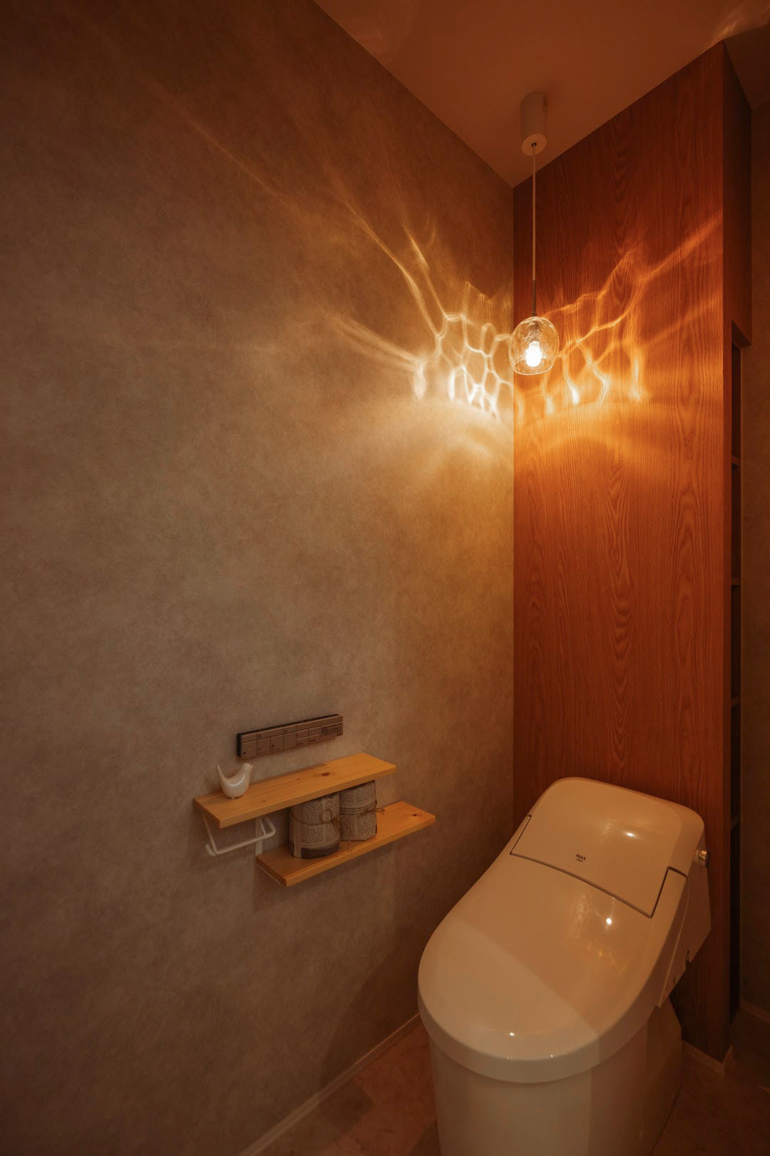 照明の陰影が壁に映える、木目を取り入れた落ち着きのあるトイレ空間